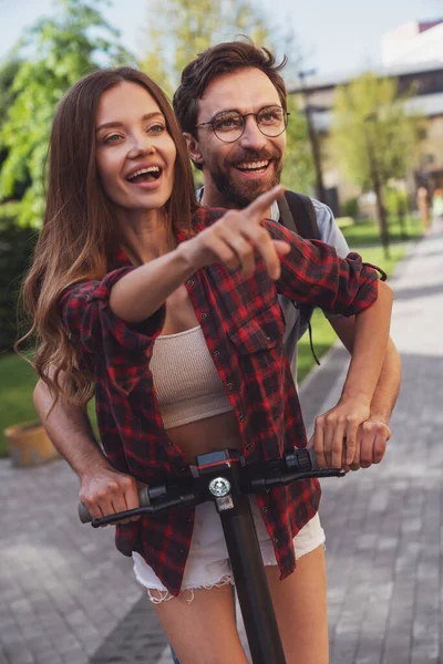 Şehrin caddesinde elektrikli scooter kullanan neşeli genç bir çift..