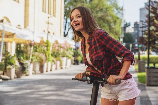 Şehrin caddesinde elektrikli scooter sürerken neşeli, genç ve güzel bir kız..
