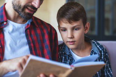 Mutlu küçük çocuk ve neşeli babası evdeki kanepede oturmuş kitap okuyorlar..