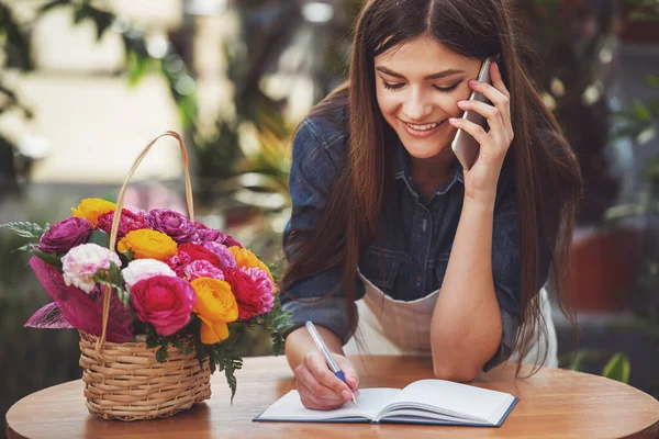 年轻女花商的肖像在花店打电话和做笔记 — 图库照片
