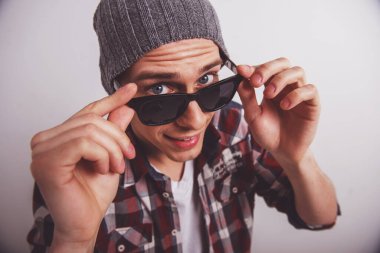 Güneş gözlüklerini ayarlayan ve gri arka plana karşı dururken kameraya bakan genç adamın üst görünümü.