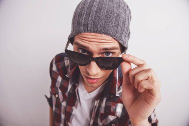 Güneş gözlüklerini ayarlayan ve gri arka plana karşı dururken kameraya bakan genç adamın üst görünümü.