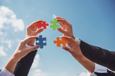 Dört parça yapbozu bir araya getirmek isteyen iş adamlarının yakın çekimi. Gökyüzü arka planı.