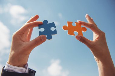 İki parça yapbozu bir araya getirmek isteyen iş adamlarının yakın çekimi. Gökyüzü arka planı.