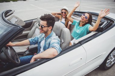 Güneş gözlüğü cabriolet seyahat üç mutlu arkadaş. İki kız arka koltuklarda eğleniyor.