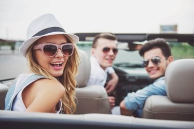 Güneş gözlüğü ve cabriolet oturan, kameraya bakıyor ve onun erkek arka plan üzerinde karşı gülümseyen şapka neşeli kadın.