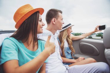 Üç güzel arkadaş Cabriolet arka koltuklar üzerinde otururken selfie alarak. Yan görünüm.