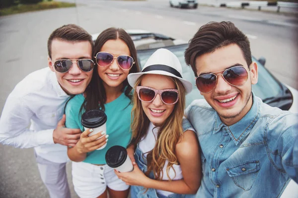 Kameraya bakarak ve gülümseyen cabriolet yakınındaki iki güzel çiftler. Kahve tutan kızlar.