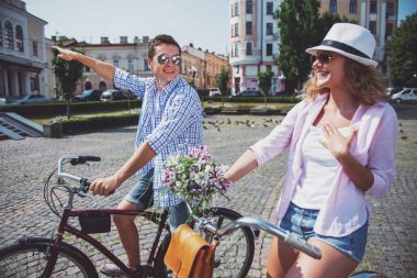 Mutlu çift güneş gözlüğü şehrin sokak bisiklet sürme. Uzağa işaret eden adam.