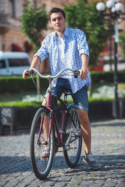 年轻男子骑着自行车在城市大街上 看着相机 — 图库照片