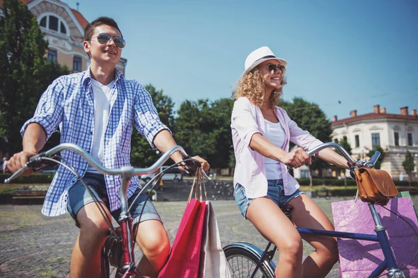 街で自転車に乗って買い物袋とサングラスで幸せなカップル — ストック写真