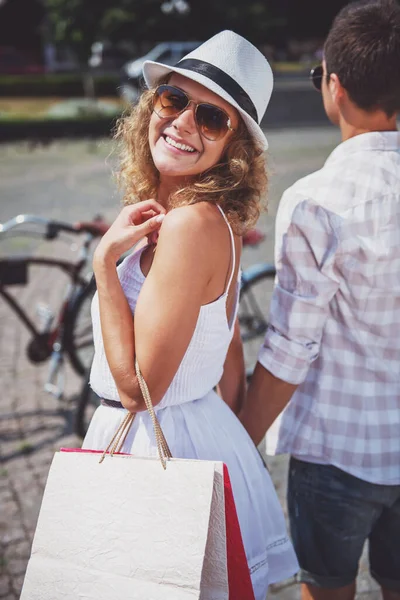 きれいな女性の持株のショッピング バッグ カメラ目線と笑顔ながら背景の上に立って彼女のボーイ フレンド — ストック写真