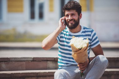 Yakışıklı genç adam akıllı rahat kıyafet buket çiçek ve bekleyen kız tutuyor.