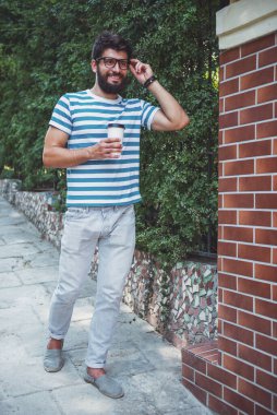 Genç adam bir fincan kahve tutarak ve yürüyüş.