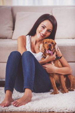 Gülümseyen genç kadın köpeğiyle evde eğleniyor.