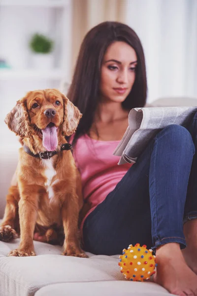 彼女の犬は彼女の近くのソファに座っている間に若い女性の写真が新聞を読んでいます — ストック写真