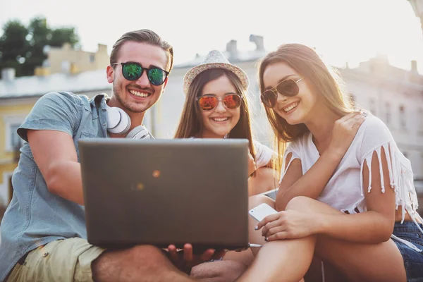 Friendship, leisure and people concept. Young people having a good time together, using laptop, sitting outdoors, in the town.