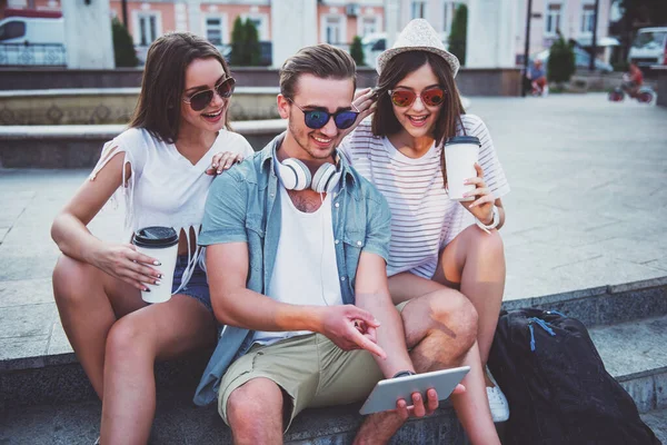 Friendship, leisure and people concept. Young people having a good time together, using digital tablet, sitting outdoors, in the town.