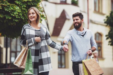 Şehirde yürürken alışveriş torbaları ile genç mutlu çift