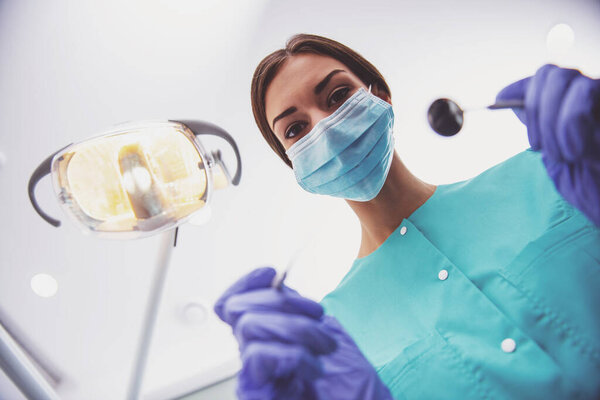 Young woman dentist in protection gloves and a mask, keeps dental instrument looking at the camera.