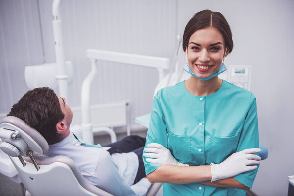 Portrait of a young dentist with folded hands, against the background of a patient  in the dental chair