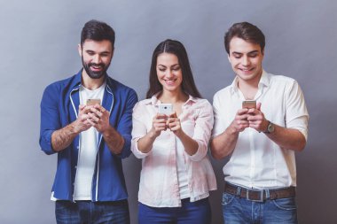 Teknoloji ve internet konsepti: gri bir arka plan üzerinde, akıllı telefonlarına bakan bir grup genç