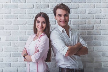 Stüdyoda poz veren genç bir çift, duygularını ve hareketlerini ifade ediyor, gülümsüyor, tuğla bir duvarın arkasında.