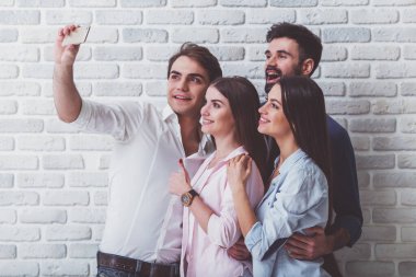 Anı yakalamak. Tuğla duvar arka planda dururken birbirlerine bağlanan ve akıllı telefonda selfie çeken dört neşeli gencin üst görünümü