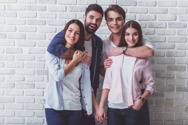 Rahat giysiler içinde mutlu arkadaşlar Portresi, sarılma, bir tuğla duvarın arka planda kamera bakarak