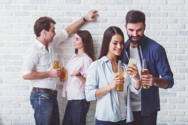Gülümseyen genç çift bir şişe bira ve bir akıllı telefon tutan, bir tuğla duvar arka planda arka planda bir şişe bira ile diğer genç bir çift