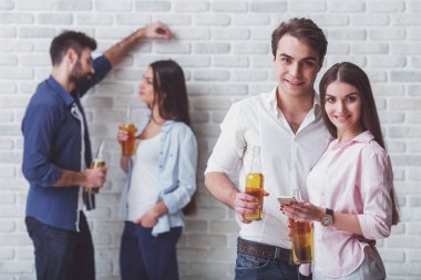 Gülümseyen genç çift bir şişe bira ve bir akıllı telefon tutan, bir tuğla duvar arka planda arka planda bir şişe bira ile diğer genç bir çift