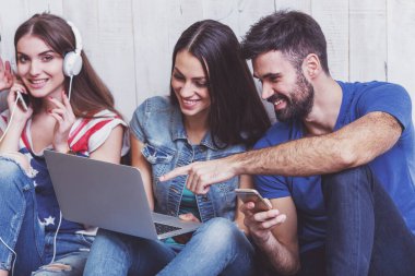 Kat bir dizüstü bilgisayar, Tablet Pc, akıllı telefonlar, müzik dinlerken kulaklık kullanarak üzerinde oturan çekici genç insanlar grup gülümseyen