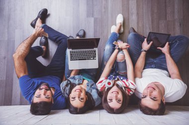 Kat bir dizüstü bilgisayar, Tablet Pc, akıllı telefonlar, müzik dinlerken kulaklık kullanarak üzerinde oturan çekici genç insanlar grup gülümseyen