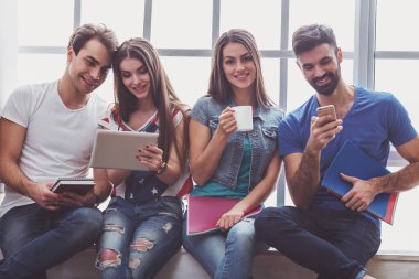 Tablet bilgisayar, Kupası, smartphone ve dizüstü bilgisayar, el altında tutmak dört genç çekici insanlar oturmak pencere kenarında, gülümseyen