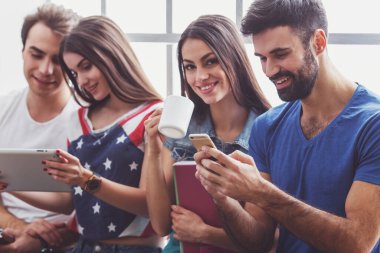 Tablet bilgisayar, Kupası, smartphone ve dizüstü bilgisayar, el altında tutmak dört genç çekici insanlar oturmak pencere kenarında, gülümseyen