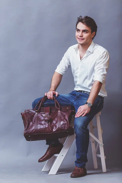 茶色の革のバッグ 白シャツと灰色の背景にブルー ジーンズの若いビジネスマン — ストック写真