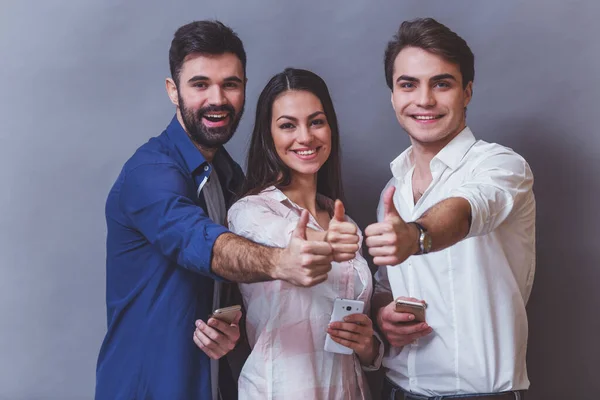 Grupo Jóvenes Atractivos Sosteniendo Smartphone Mirando Cámara Sonriendo Mostrando Pulgares — Foto de Stock