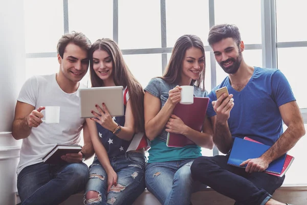 Tablet bilgisayar, Kupası, smartphone ve dizüstü bilgisayar, el altında tutmak dört genç çekici insanlar oturmak pencere kenarında, gülümseyen