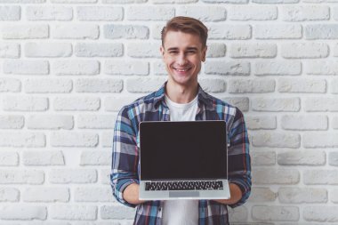 Bir dizüstü bilgisayar ile beyaz bir duvar arka planı elinde duran, kamera arıyorum güzel gülen adam