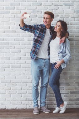 Mutlu genç çift selfie, tuğla duvar arka plan üzerinde şık elbise giymiş yapar