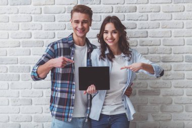 Bir tuğla duvar zemin üzerine boş siyah perde tablet parmak işaret mutlu genç Çift