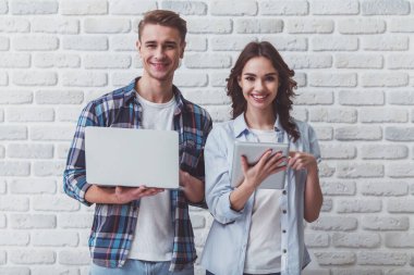 Bir dizüstü bilgisayar ve bir tablet bir tuğla duvar arka plan üzerinde genç güzel çift dur