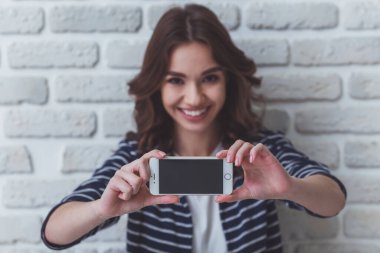 Güzel genç kadın bir smartphone bir tuğla duvar arka planda kendi portresi yapma