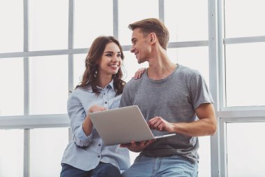 Mutlu genç çift pencere kenarında, oturup evde bir dizüstü bilgisayar kullanmak