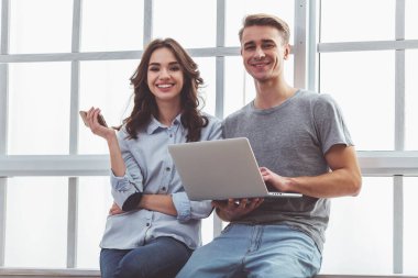 Laptop ve smartphone, ellerini tutmak gülümseyen güzel çift evde pencere kenarında oturmak