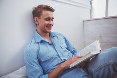 Yakışıklı delikanlı mavi tişört ve kot yastık evde yerde oturup kitap okumak