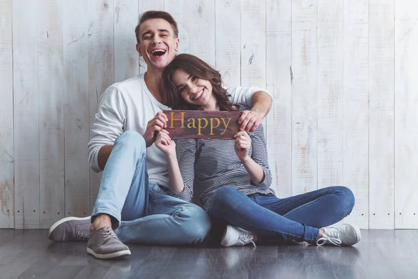 Feliz Jovem Casal Mantendo Sinal Que Diz Sentado Chão Madeira — Fotografia de Stock