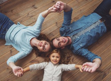 Güzel genç aile kamera bakıyor, gülümseyerek ve evde ahşap zemin üzerinde yatarken el ele tutuşuyor