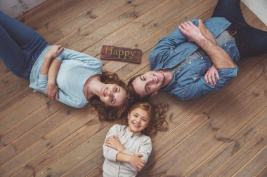 Evde ahşap zemin üzerinde yatarken kameraya bakan ve gülümseyen güzel genç ailenin üst görünümü