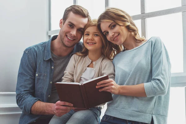 Piękne Młode Rodziny Patrząc Aparacie Uśmiechając Się Trzyma Książkę Siedząc — Zdjęcie stockowe